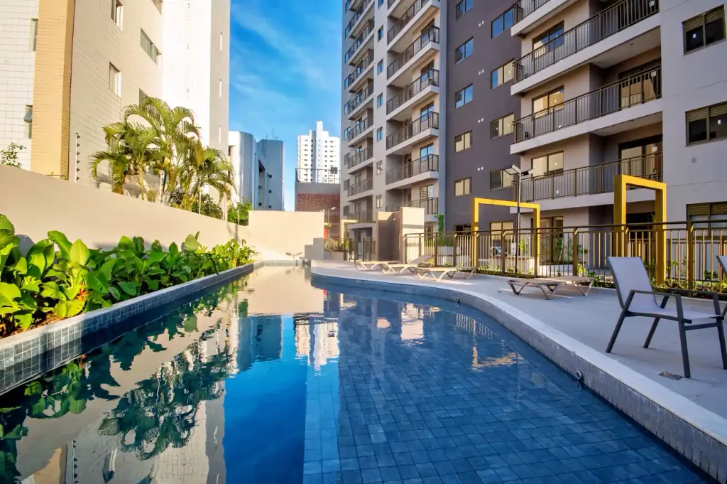 financiamento de um imóvel: Piscina em condomínio residencial com espreguiçadeiras e jardins, cercada por prédios altos em ambiente urbano, ao fundo céu azul.